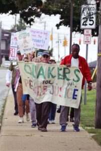 Group of Friends march with banner reading Quakers for Peace and Justice and various signs.
